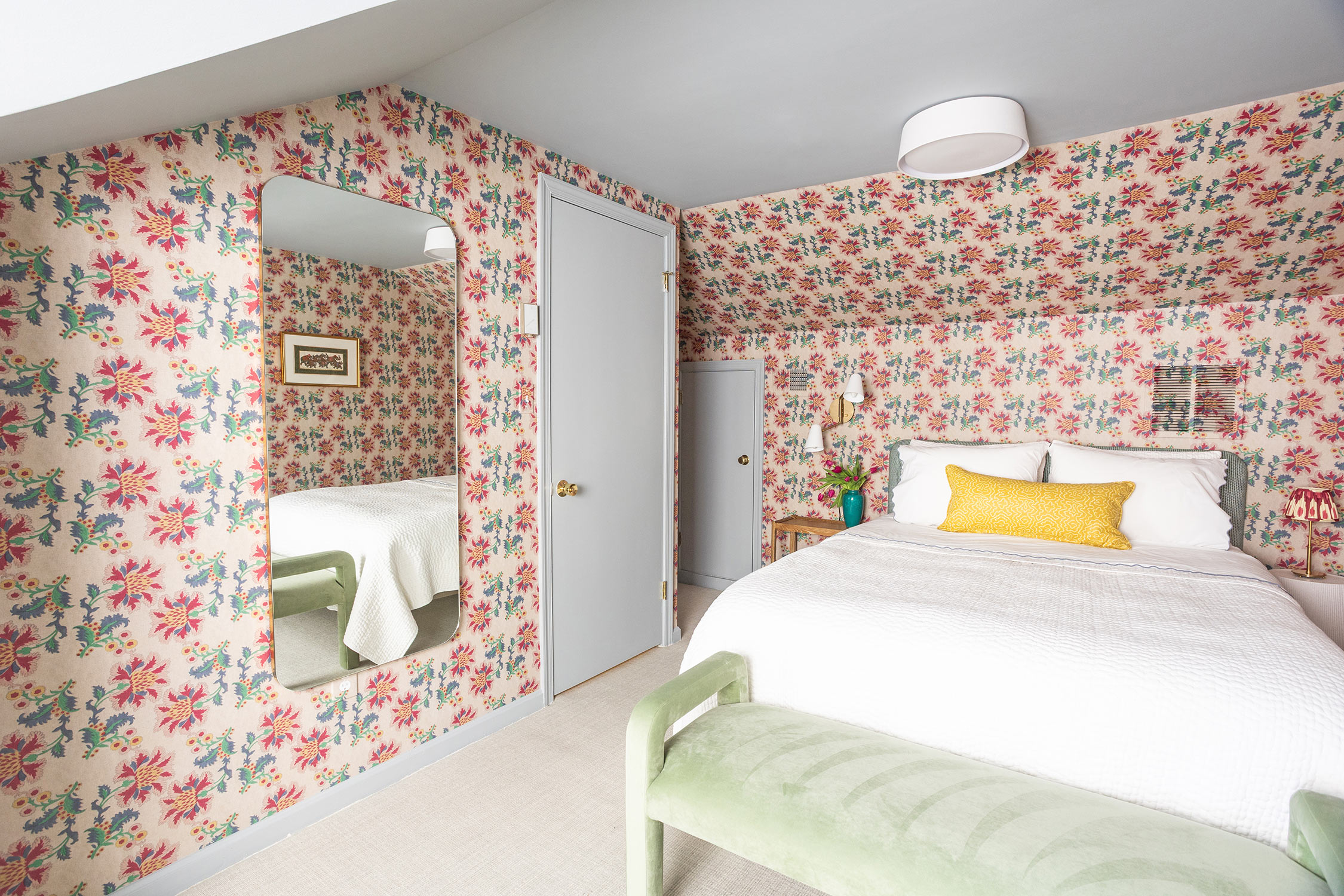Attic Guest Bedroom with colorful floral wallpaper, a bed with white bedding, gray doors and a velvet light green bench at the foot of the bed