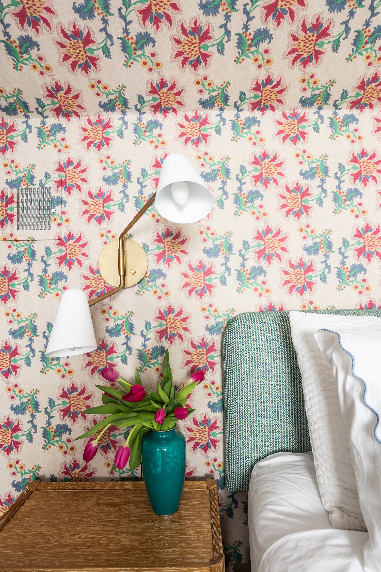 Contemporary Lamp on the side of a bed with white linen. On the night stand is a floral arrangement in an aqua vase